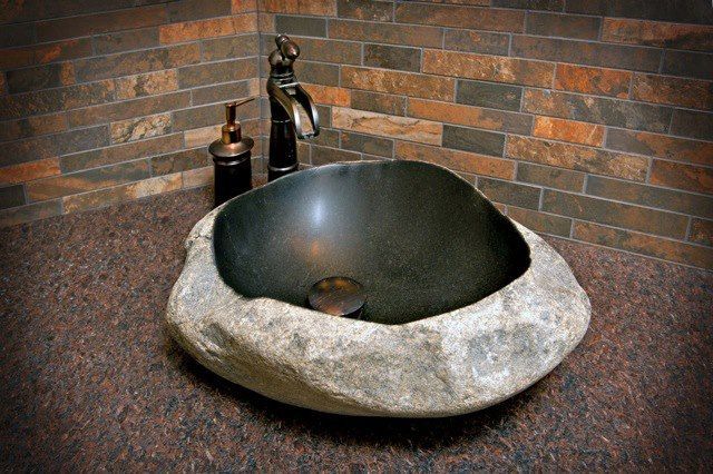 A stone sink with a faucet and soap dispenser in a bathroom.