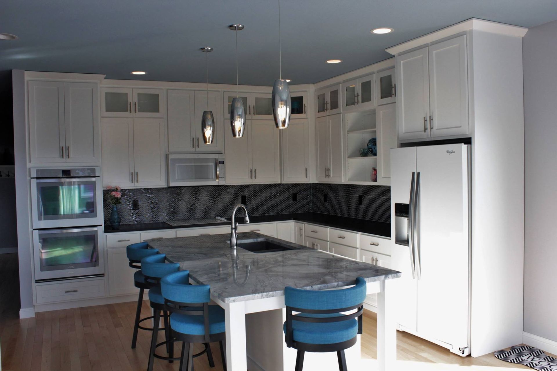 A kitchen with white cabinets and a large island with blue chairs.