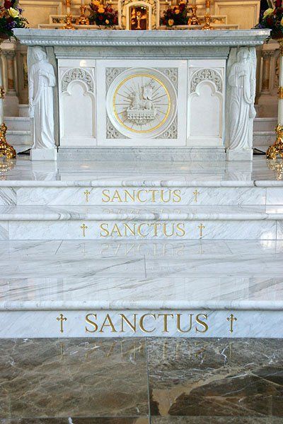 A white marble altar in a church with the words sanctus written on the steps.