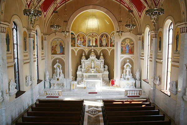 The inside of a church with rows of wooden benches and a large altar.