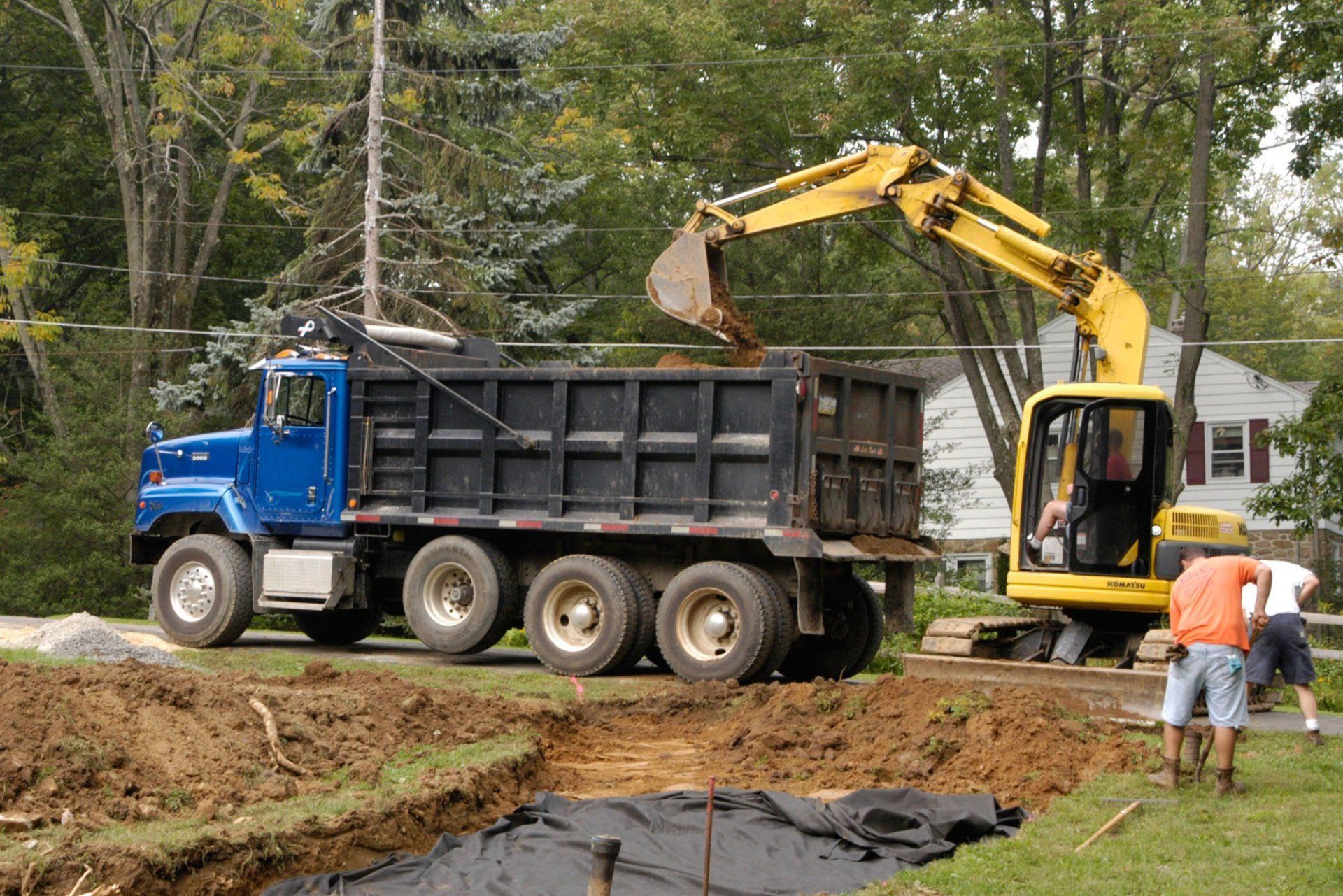 A dump truck is being loaded with dirt by a yellow excavator.