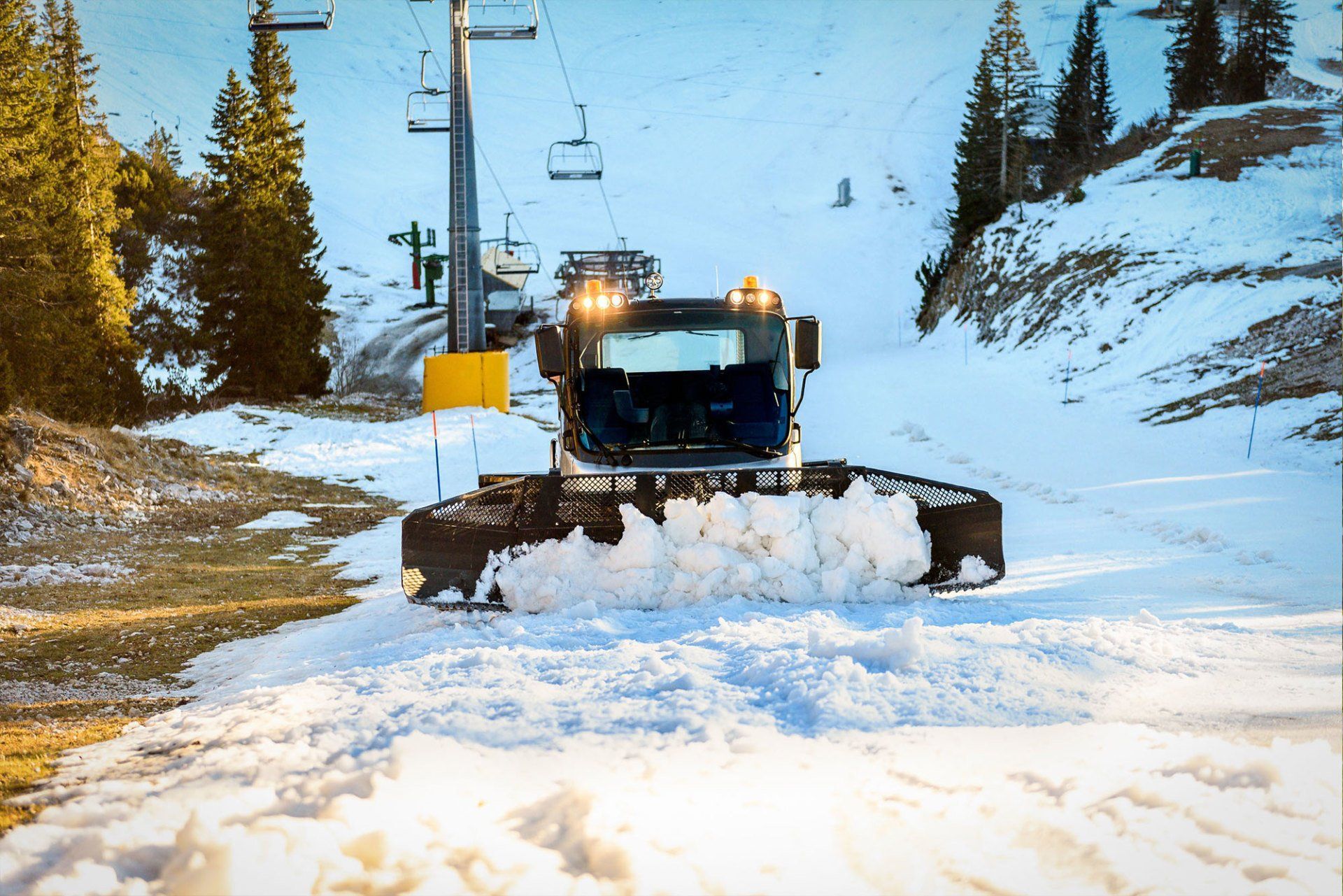 A snow plow is clearing snow from a ski slope.