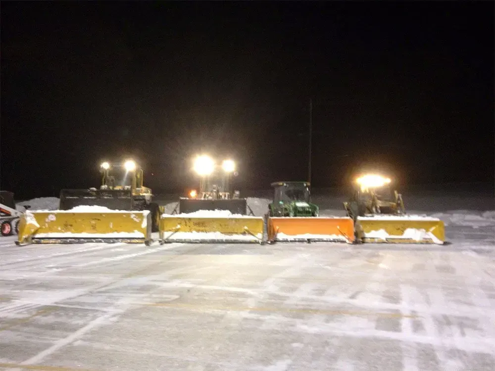 Three snow plows are lined up in a parking lot at night.