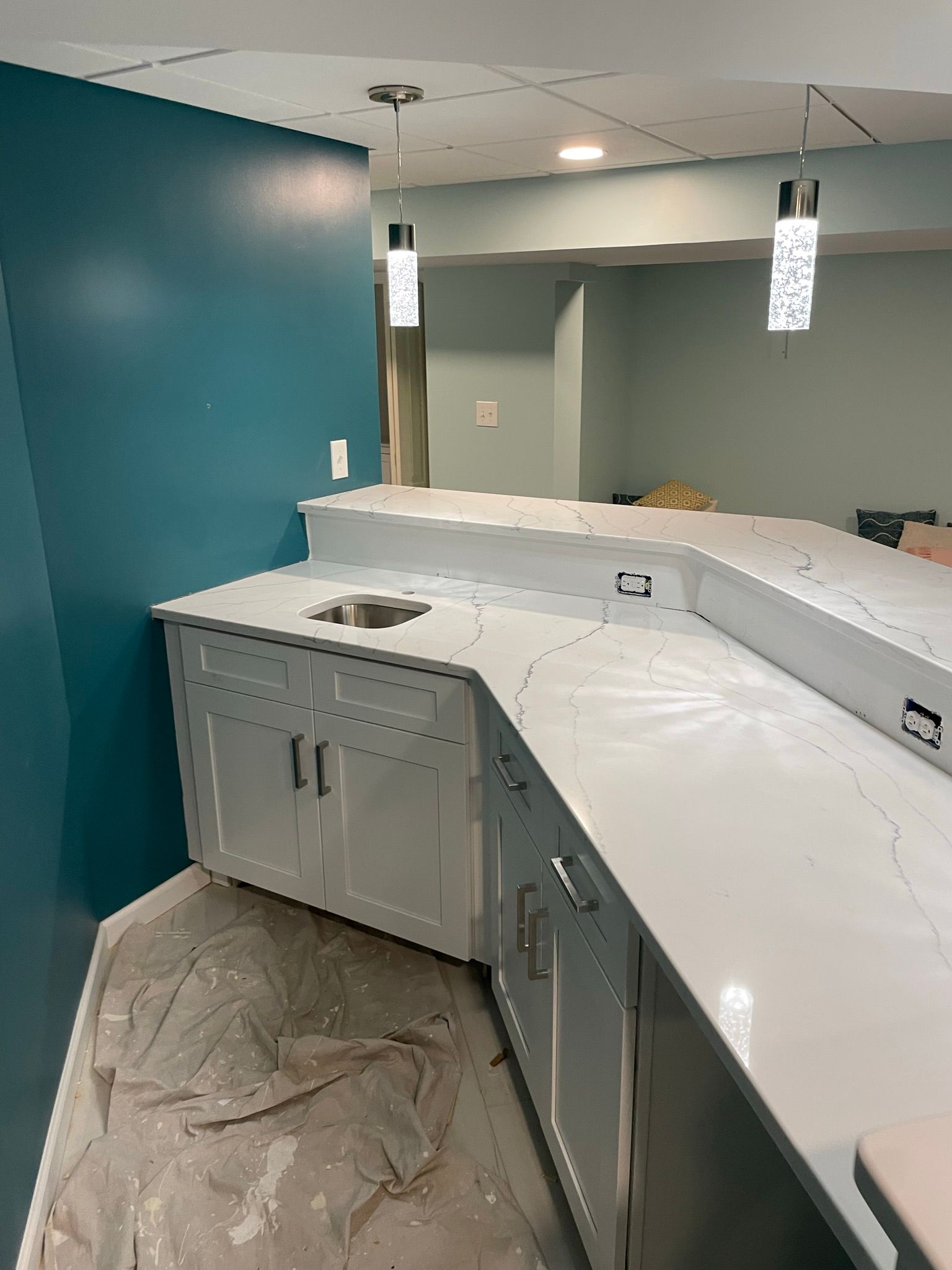 Basement bar with white countertops, blue accent wall, and pendant lights.