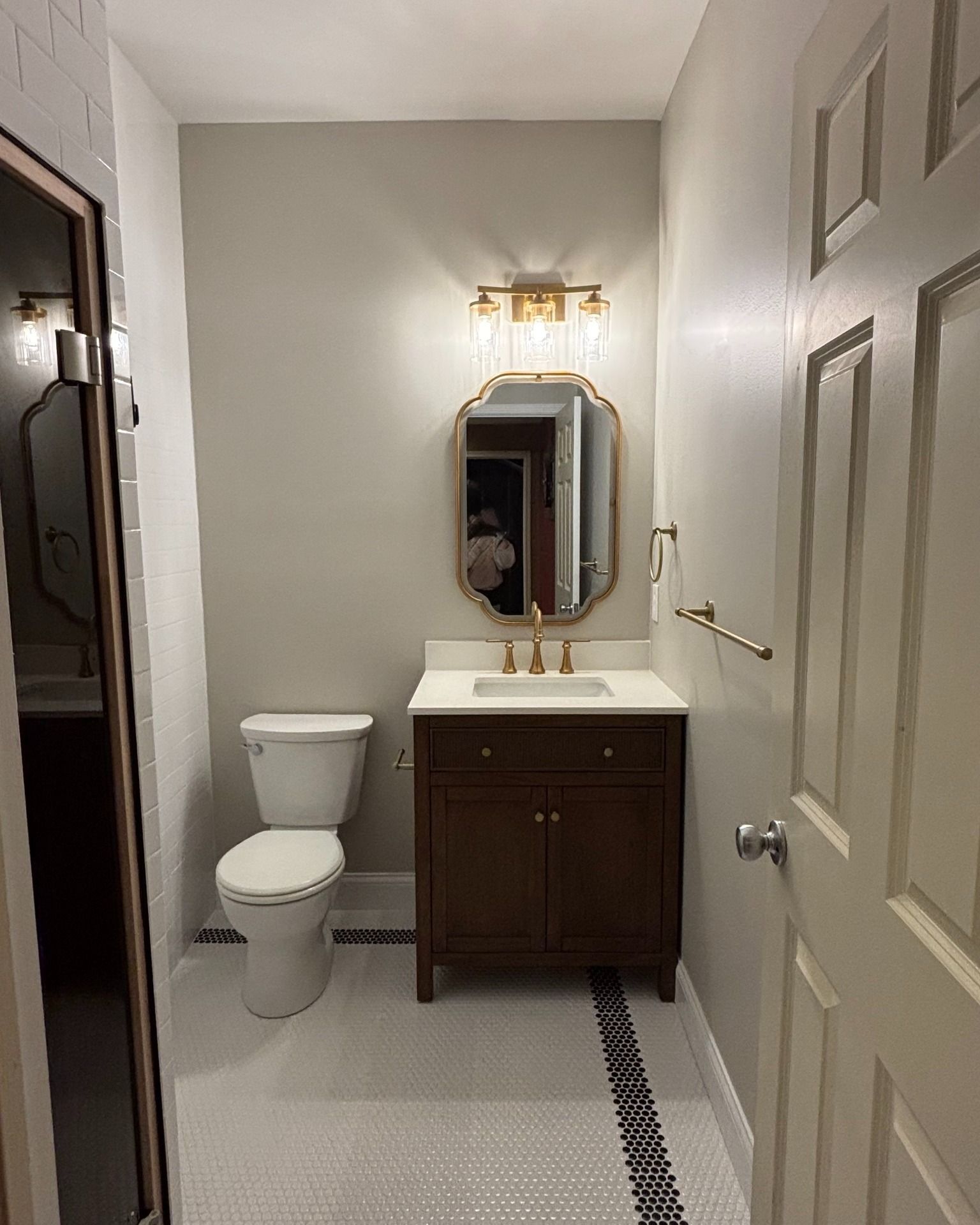 Bathroom with toilet, vanity, mirror, gold fixtures, and black and white tile flooring.