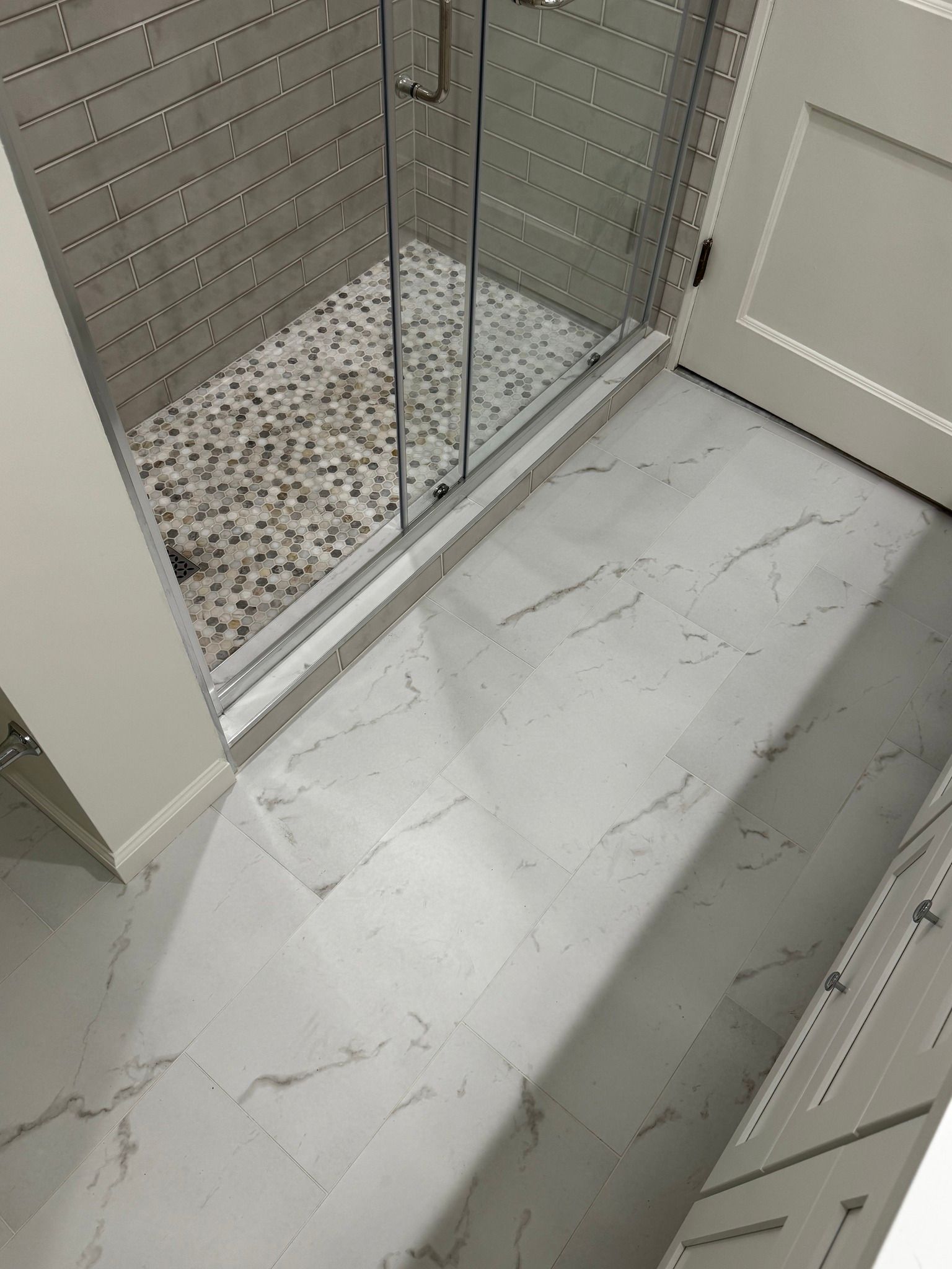 Bathroom with white marble-look floor and glass shower enclosure.