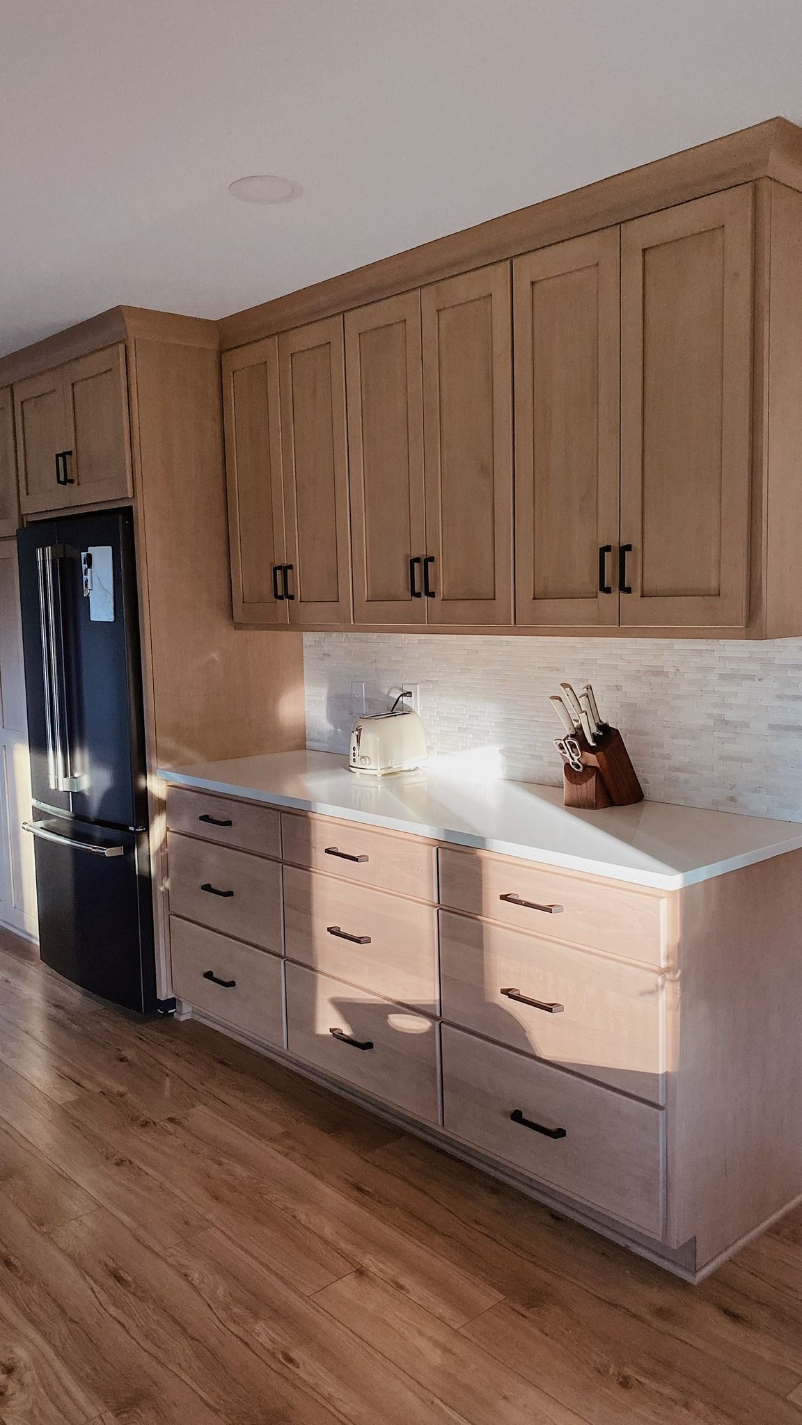 Kitchen with light wood cabinets and countertops, black appliances, and hardware.