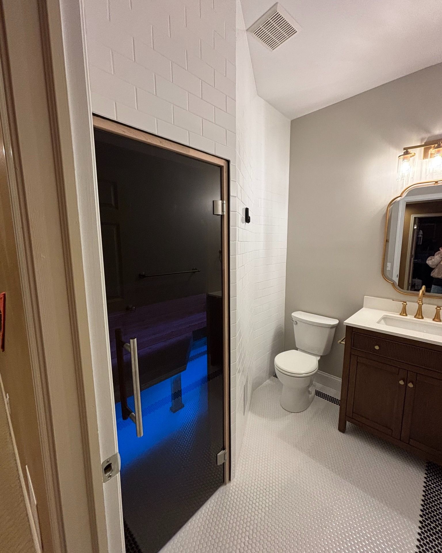 Bathroom with a dark-glassed sauna, toilet, vanity, and a white, textured tiled floor.