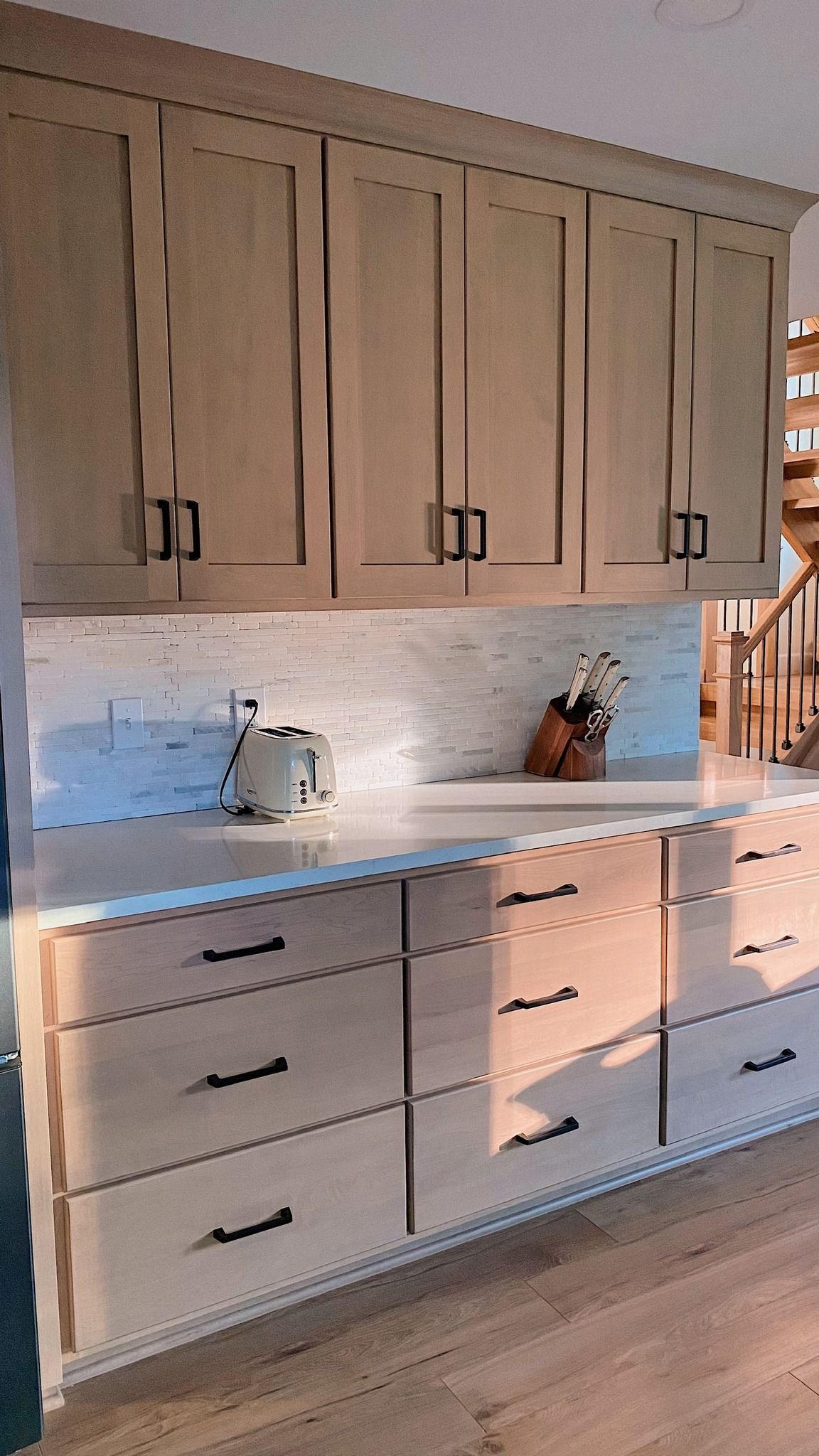 Light wood kitchen cabinets and drawers with black hardware; white backsplash and countertops.
