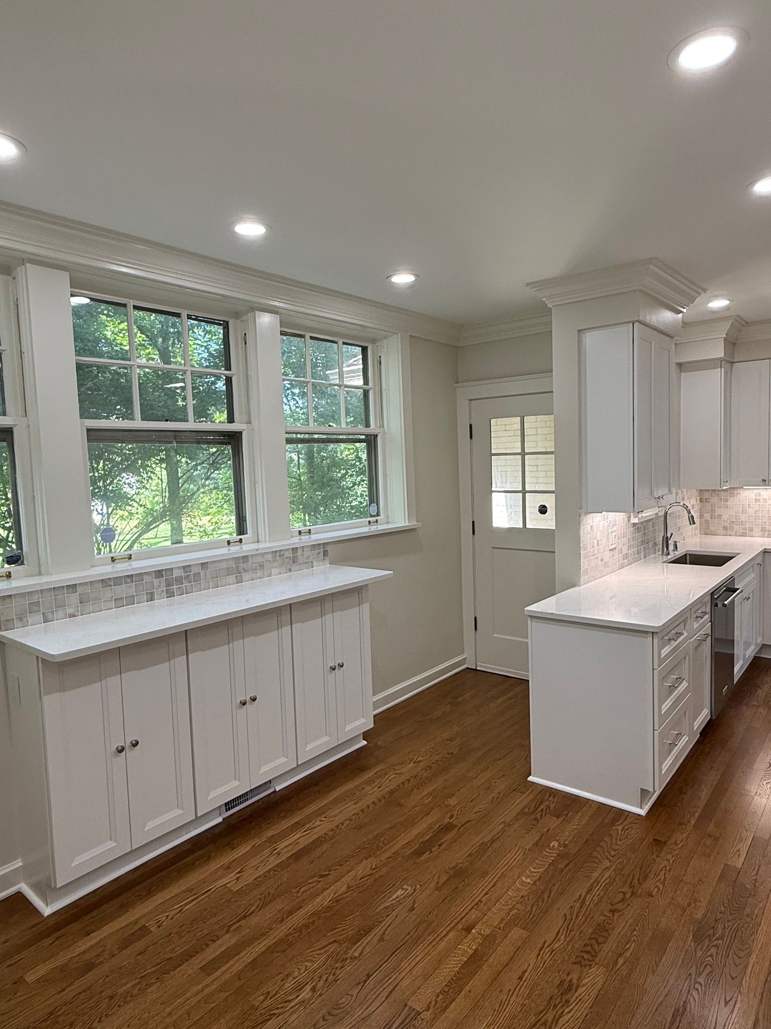 White kitchen with white cabinets, marble countertops, and hardwood floors.