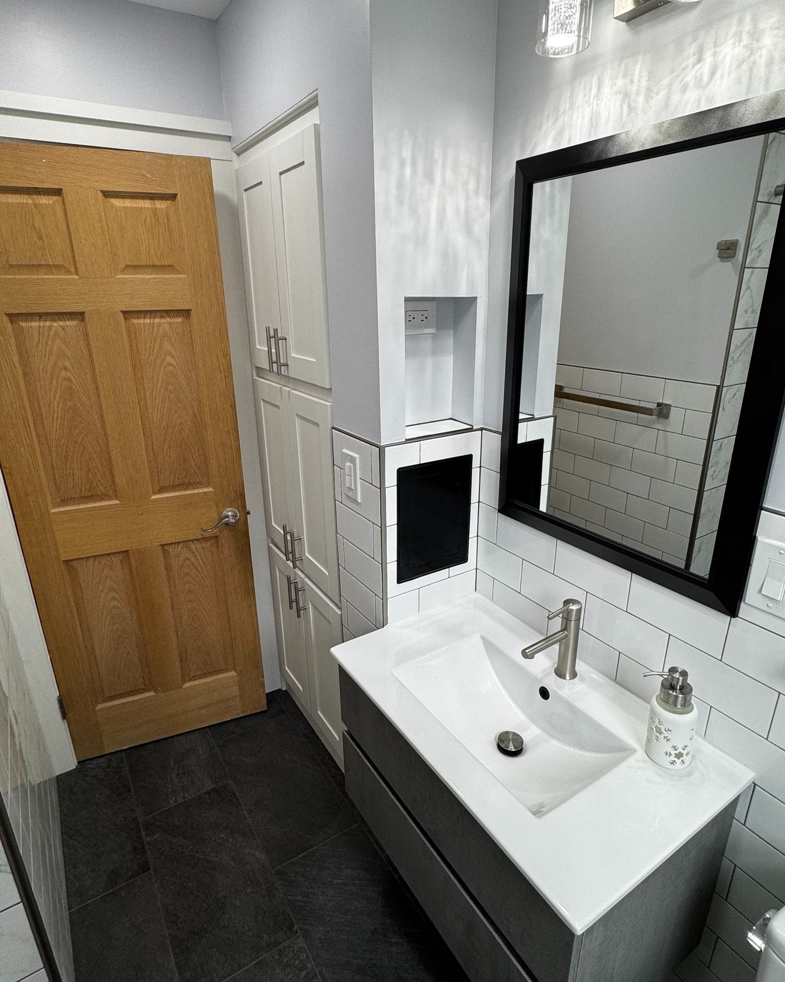 Bathroom with a white sink, black mirror, wooden door, and gray tiled floor.
