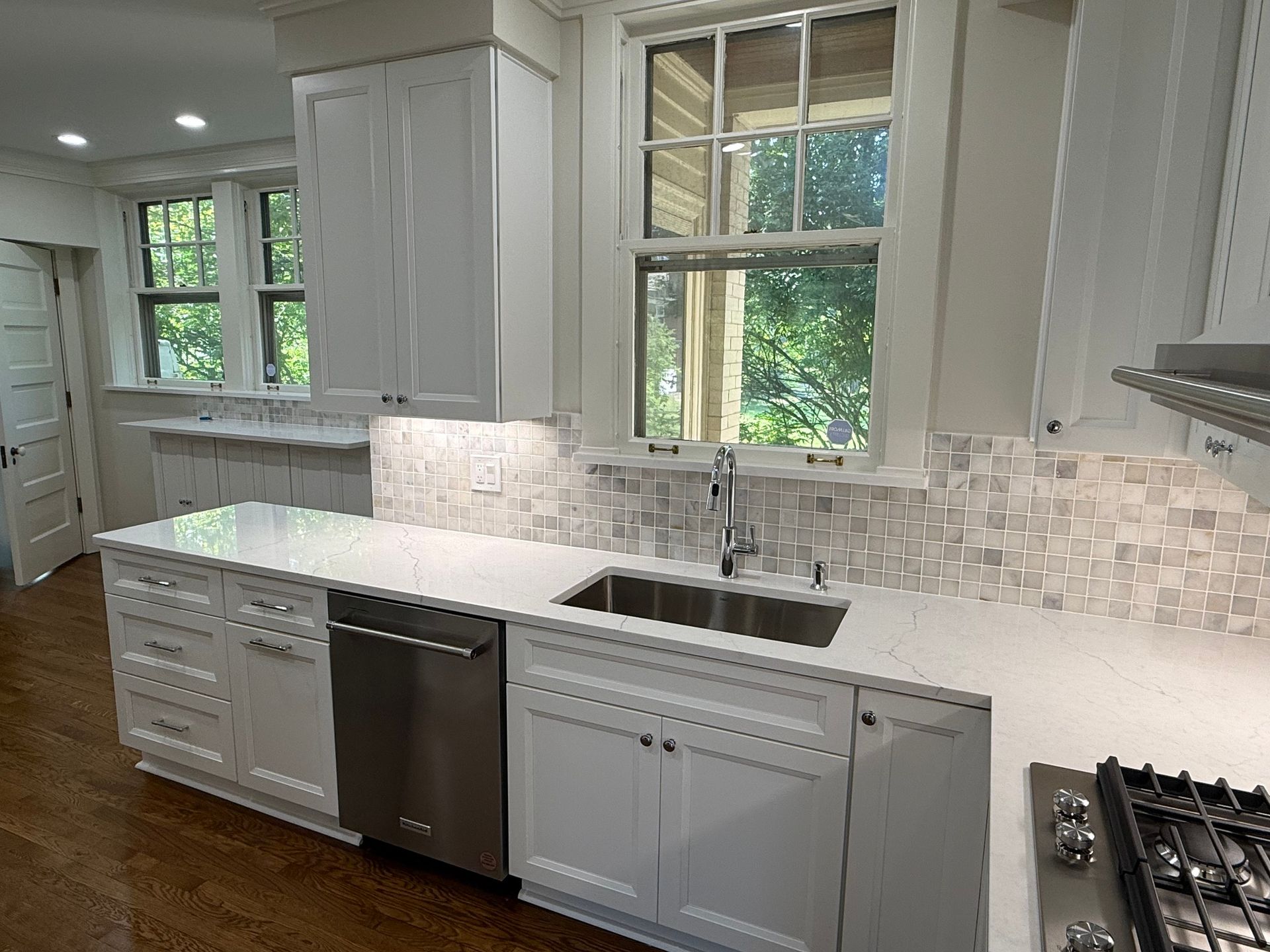 White kitchen with countertops, cabinets, and a stainless steel sink and appliances. Windows provide natural light.