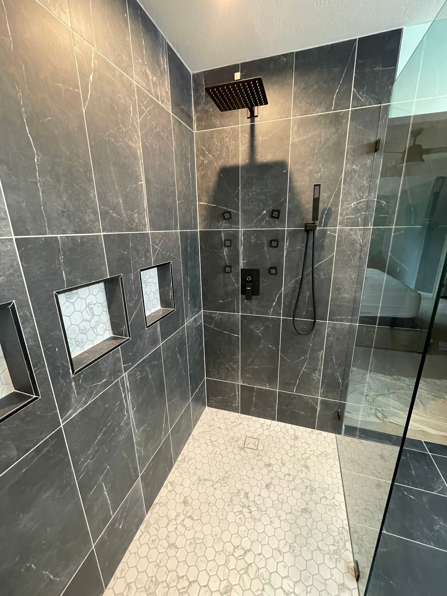 Dark tile shower with rain head, body jets, handheld shower, recessed shelves, and pebble floor.