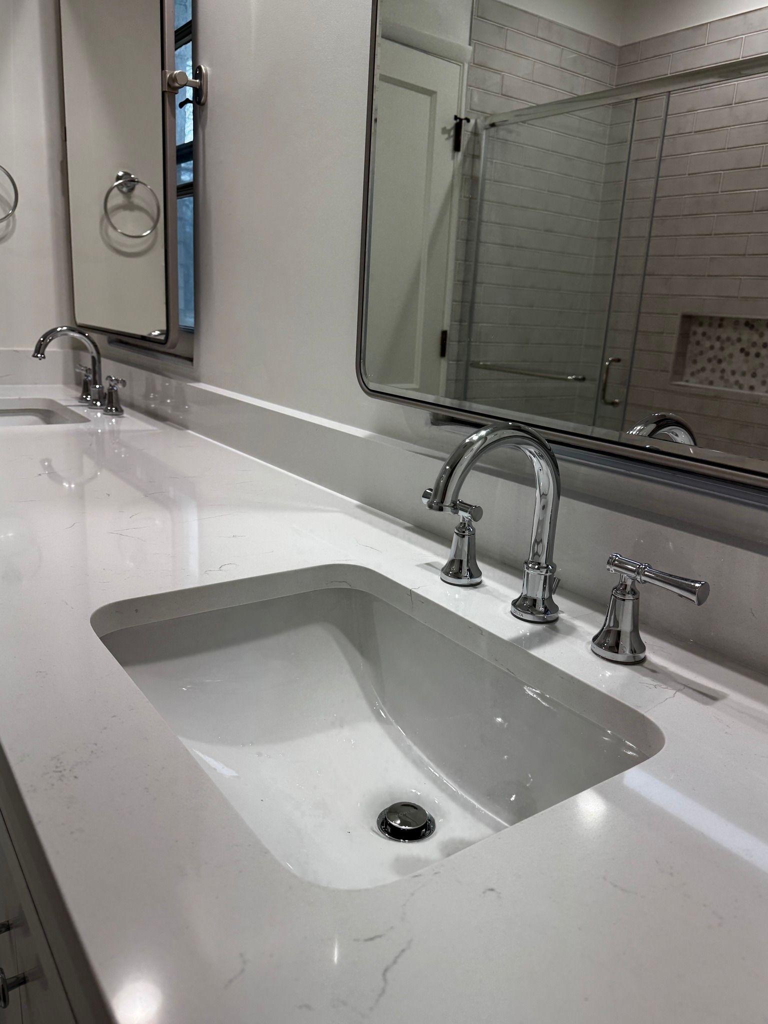 Bathroom vanity with white countertop, two sinks, chrome faucets, and a mirror.