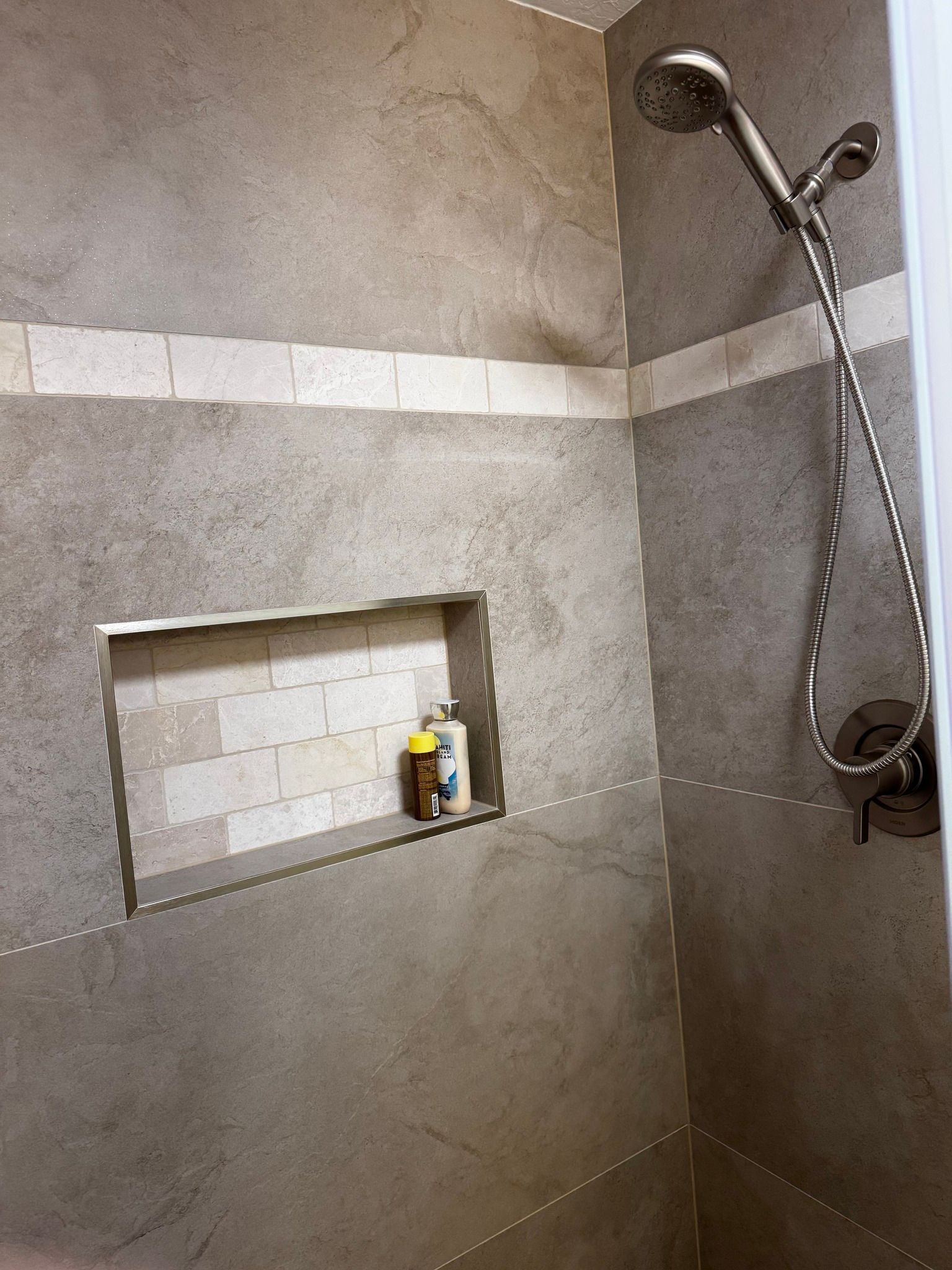 Shower with gray tiled walls, a shelf niche, and a silver showerhead.