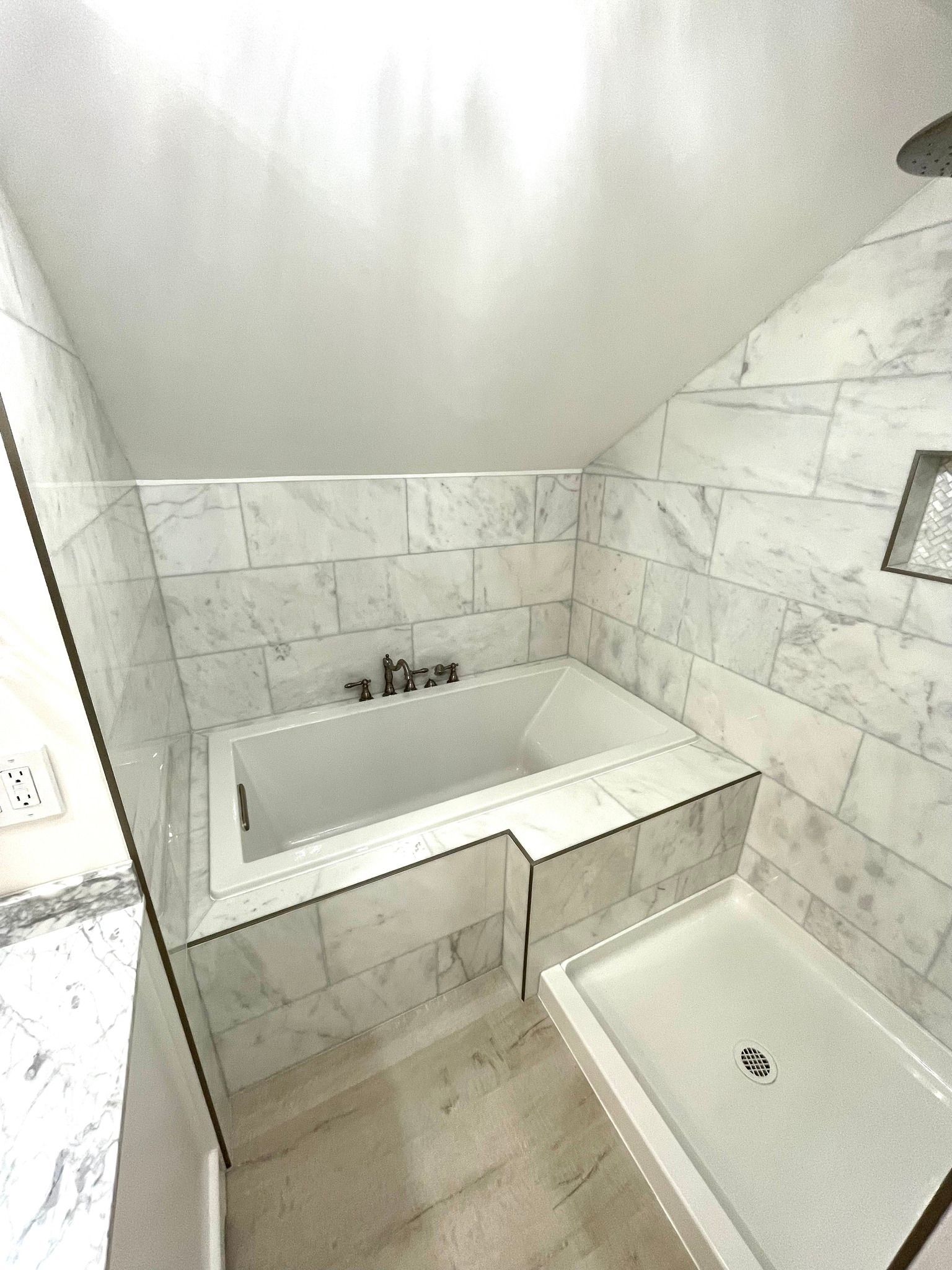 Bathroom with a white bathtub and shower enclosed by marble tile walls.