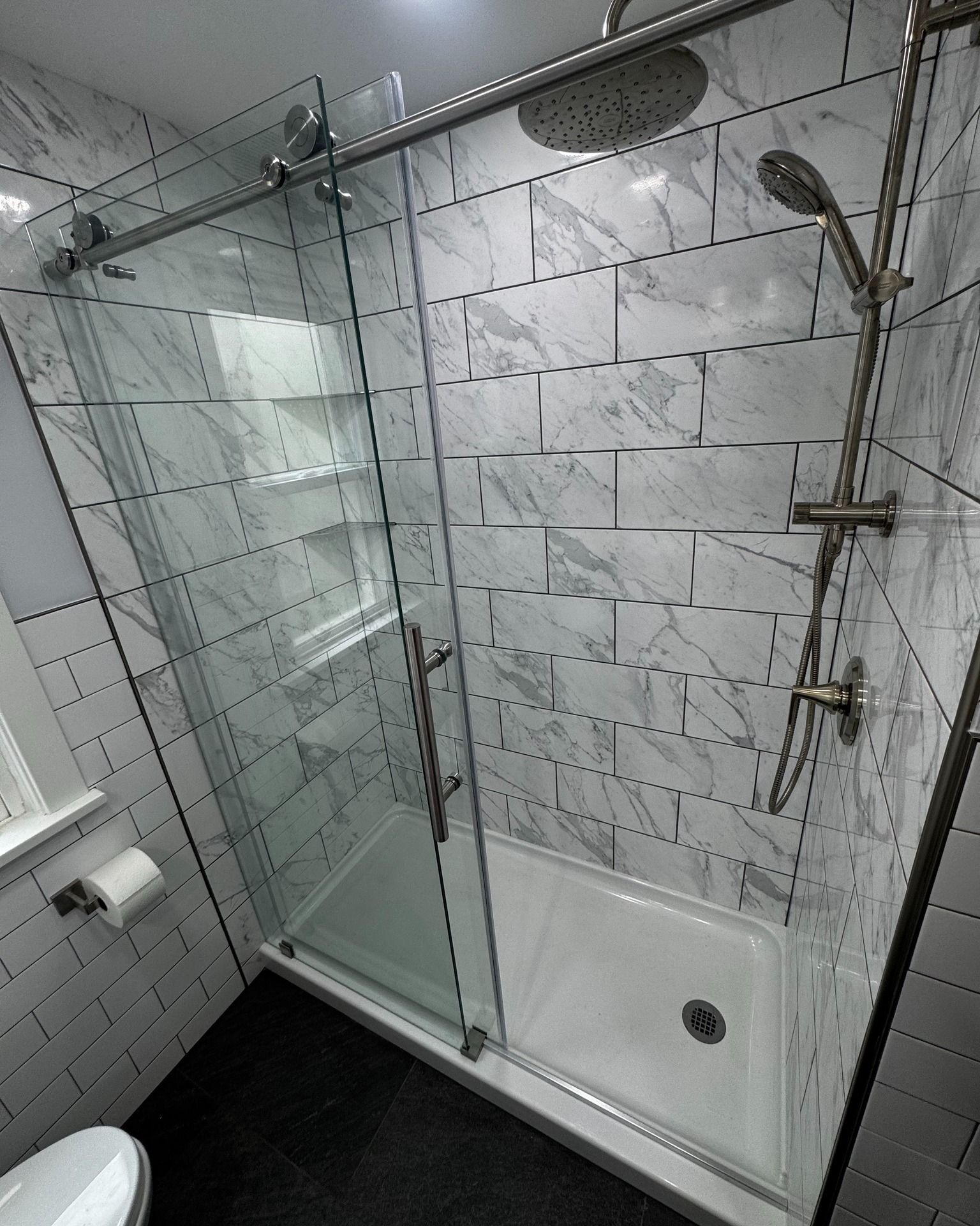 Modern bathroom shower with sliding glass doors, white marble-look tiles, and silver fixtures.