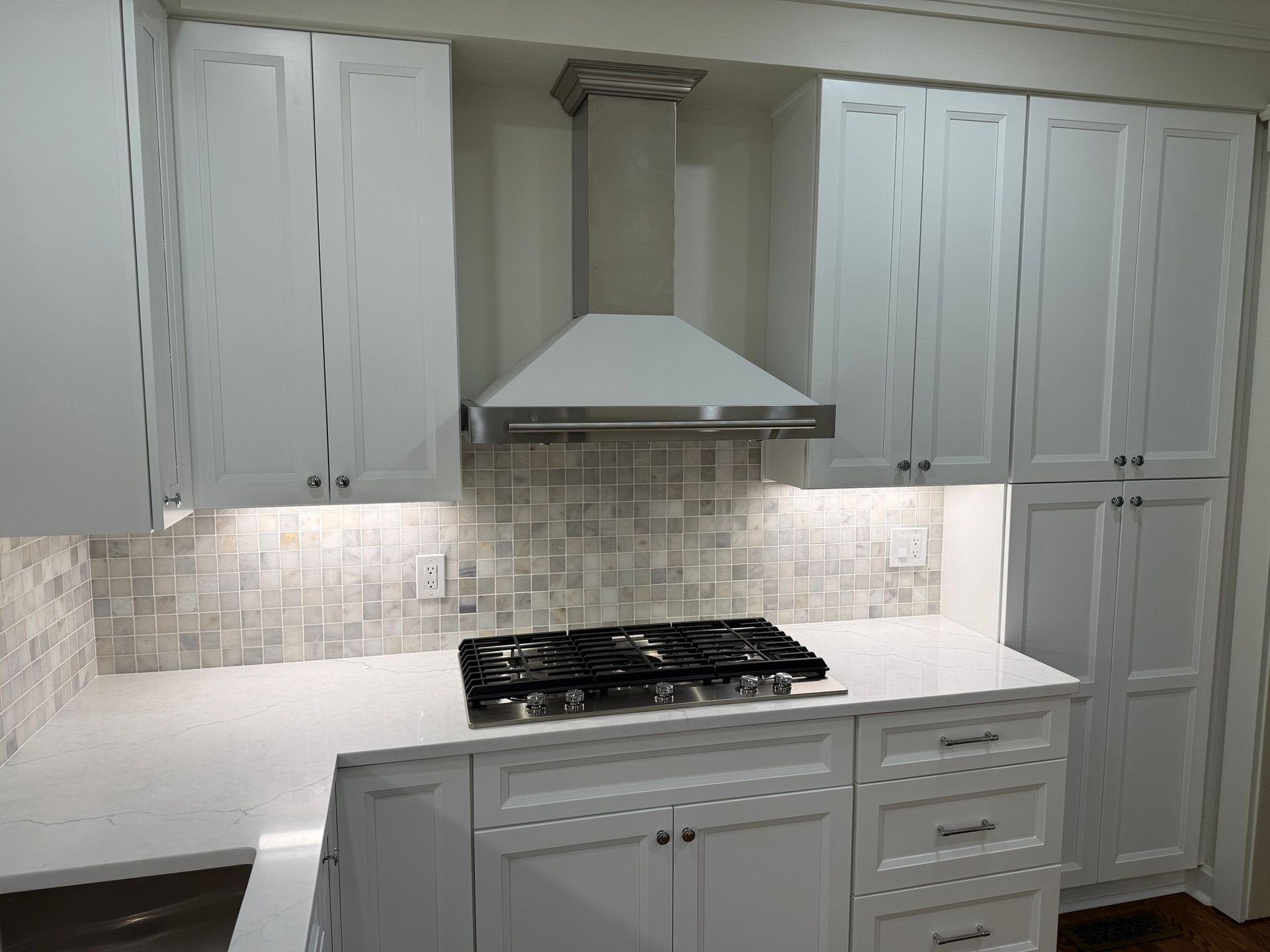 White kitchen with cabinets, stove, vent hood, backsplash, and island.