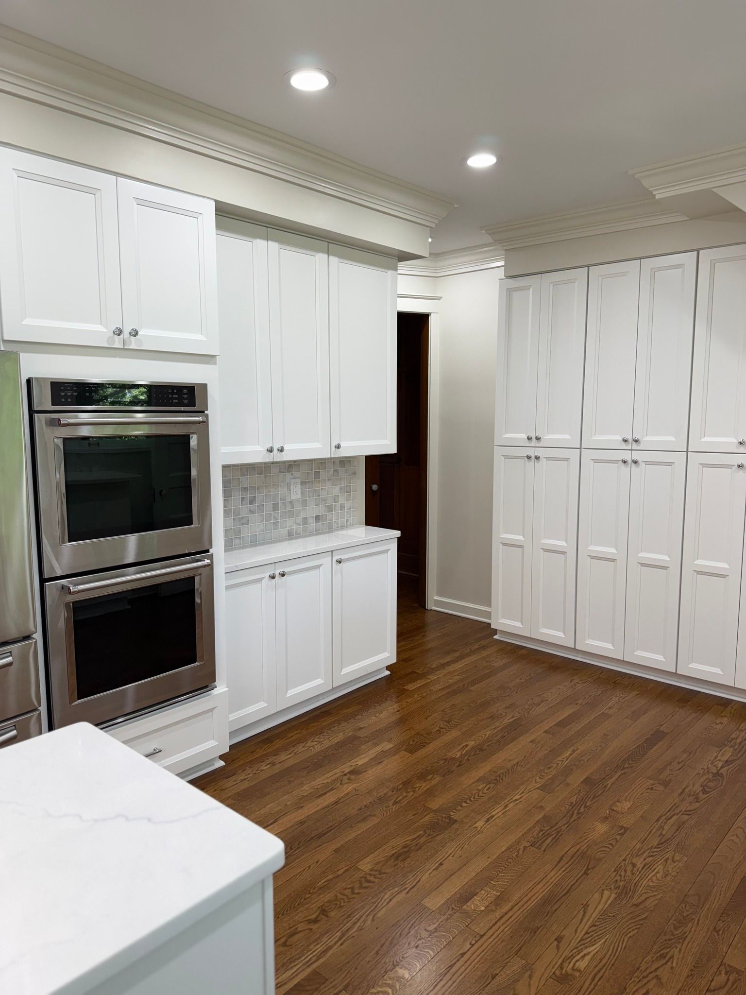 White kitchen with wood floors, stainless steel appliances, and white cabinets.
