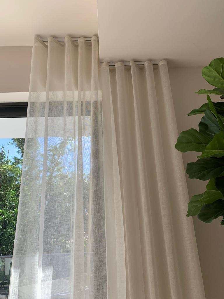 A pair of white curtains are hanging on a window next to a plant