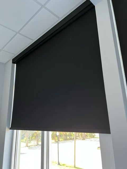 A black blind is hanging on a window in a room.