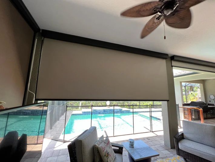 A living room with a ceiling fan and a swimming pool in the background.