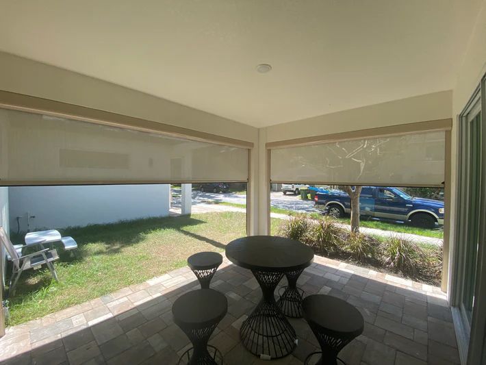 A porch with a table and stools and a car parked in the background.
