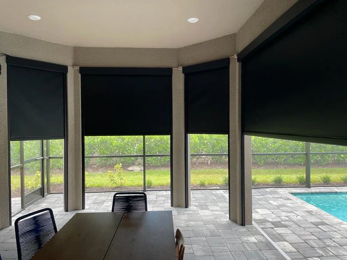 There is a table and chairs in the room with a pool in the background.