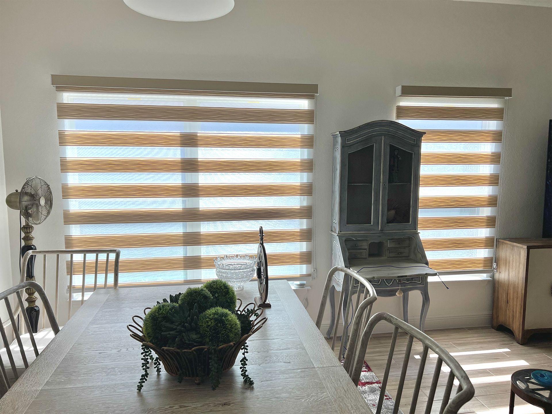 A dining room with a long table and chairs and striped blinds on the windows