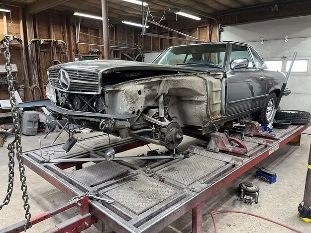 Damaged vintage Mercedes-Benz undergoing repair in a garage, on a frame straightening machine.