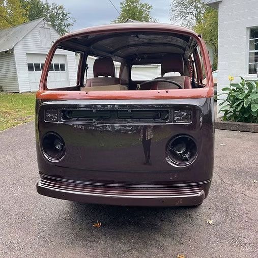 Brown Volkswagen van body; front view.  No windows or engine.  Parked on pavement near a house.