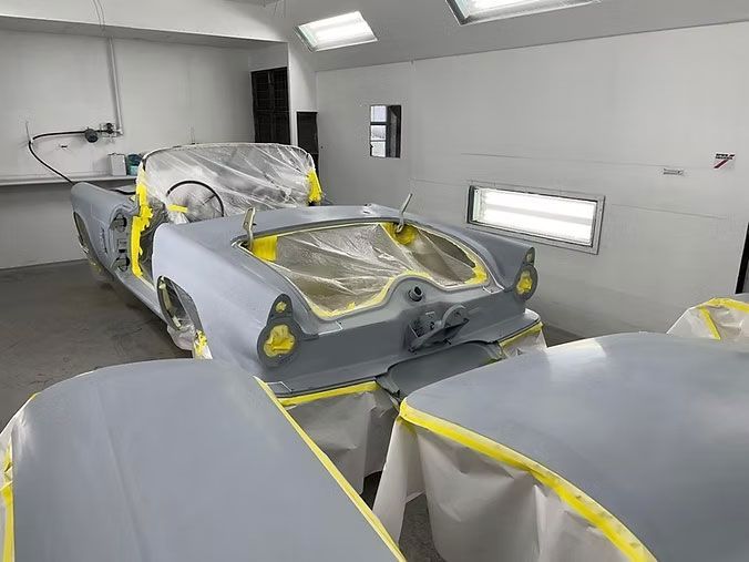 Classic car in a paint booth, taped and primed for painting.