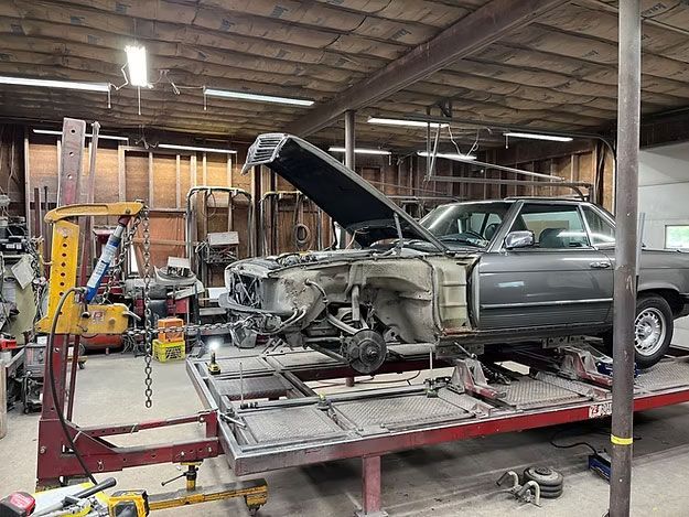 A gray car in a repair shop is on a frame machine, hood open.