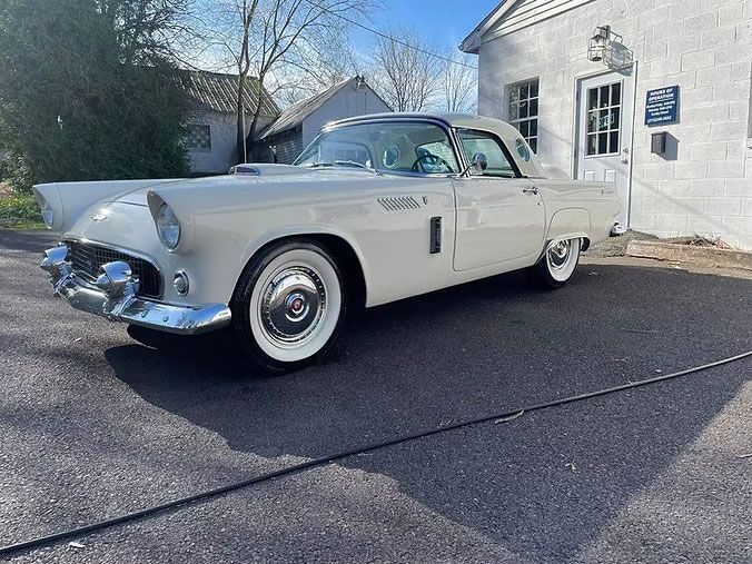 White classic Ford Thunderbird parked in front of a white building.