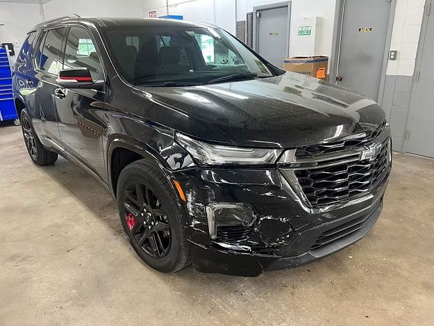 Black Chevrolet Traverse SUV with damage to the front quarter panel, in a garage setting.