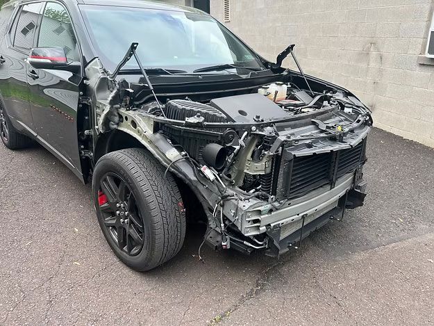 Black SUV with front-end damage, missing bumper and body panels, parked on asphalt.