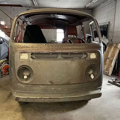 Front view of a weathered Volkswagen van frame in a garage, missing parts.