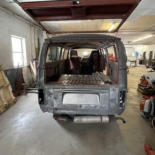 Rear view of a disassembled van in a workshop; the back door is open.