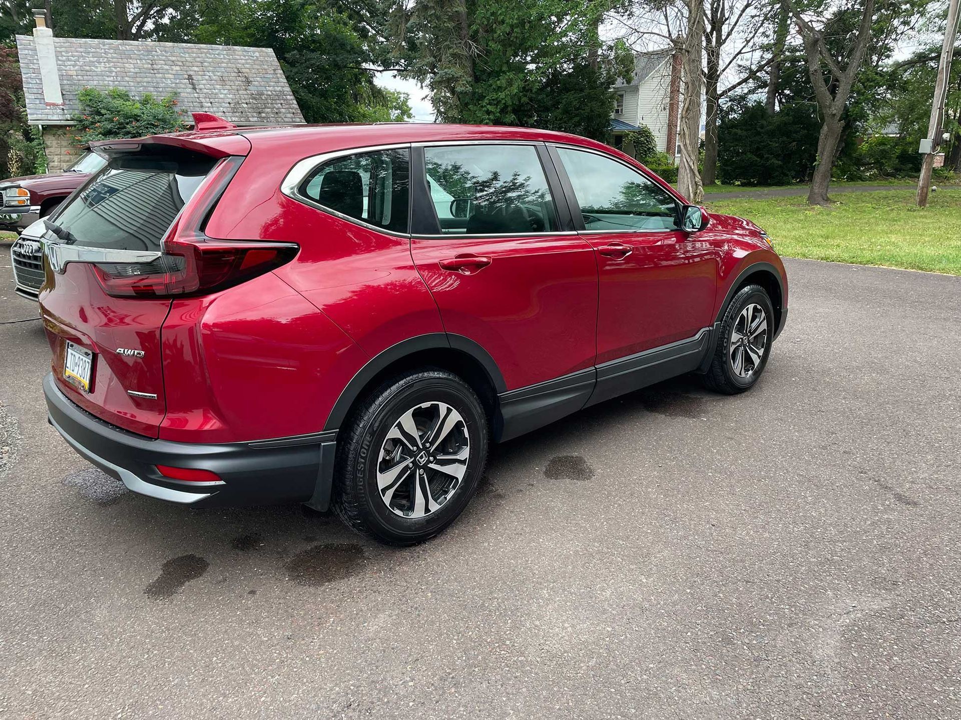 Red Honda CRV parked on an asphalt driveway, with a building and trees in the background.