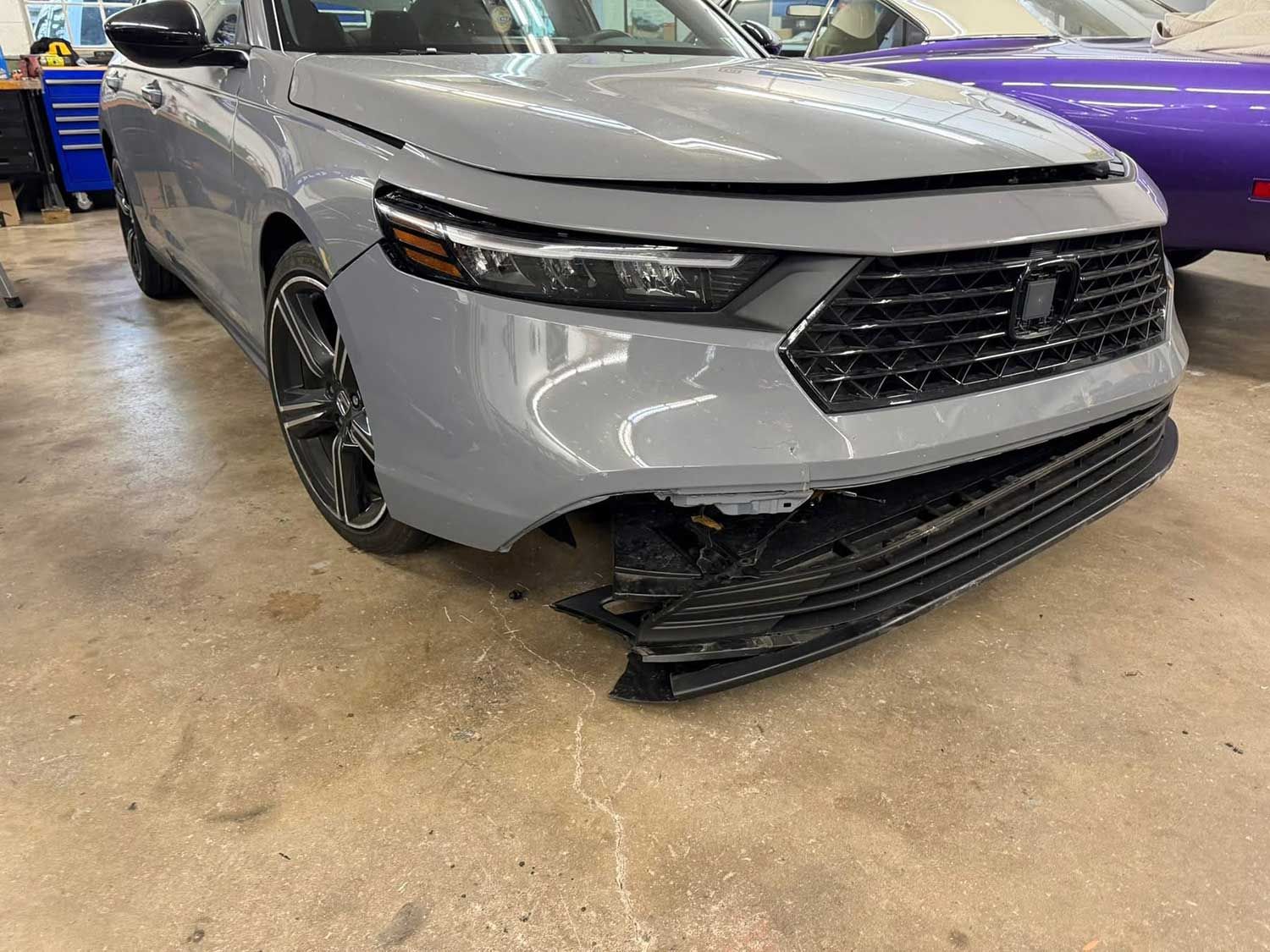 Gray car with a damaged front bumper, parked inside a garage.