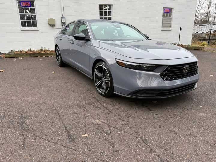 Gray sedan parked in front of a building with windows, tire tracks visible on the pavement.