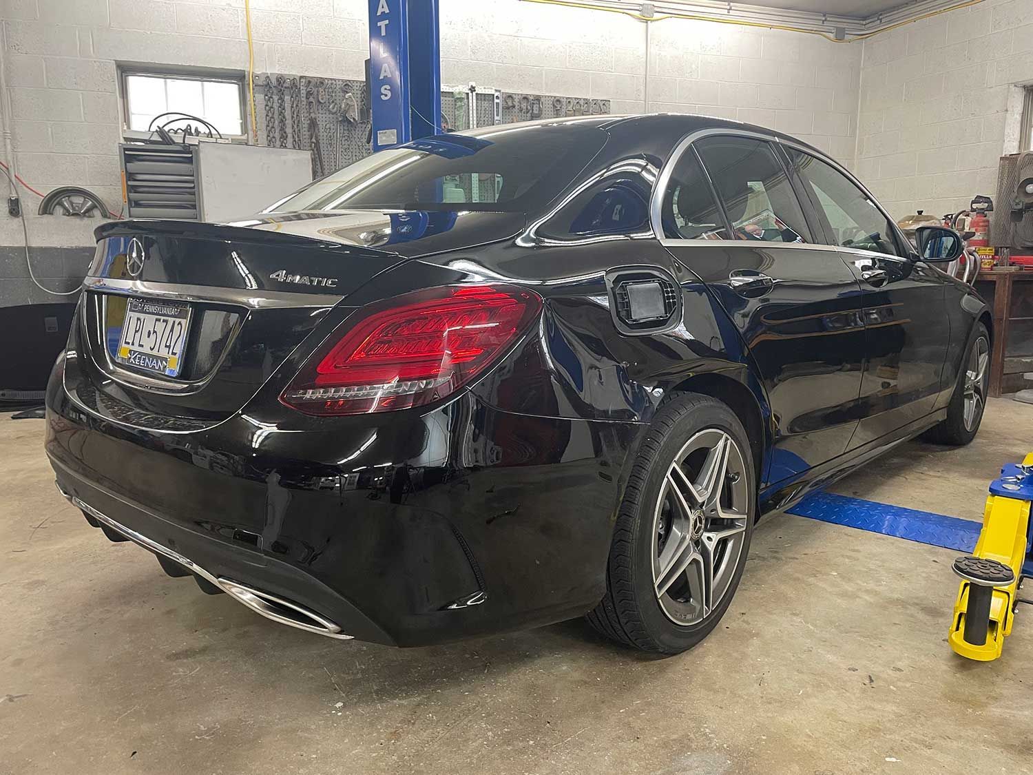 Black Mercedes sedan in a repair shop, raised on a lift.