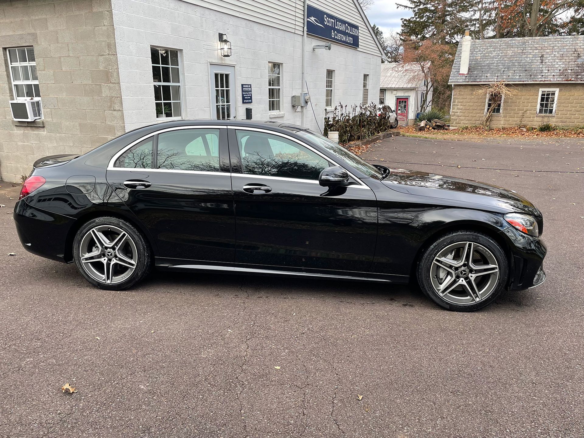Black Mercedes-Benz sedan parked in front of a white building with several windows. Pavement in foreground.