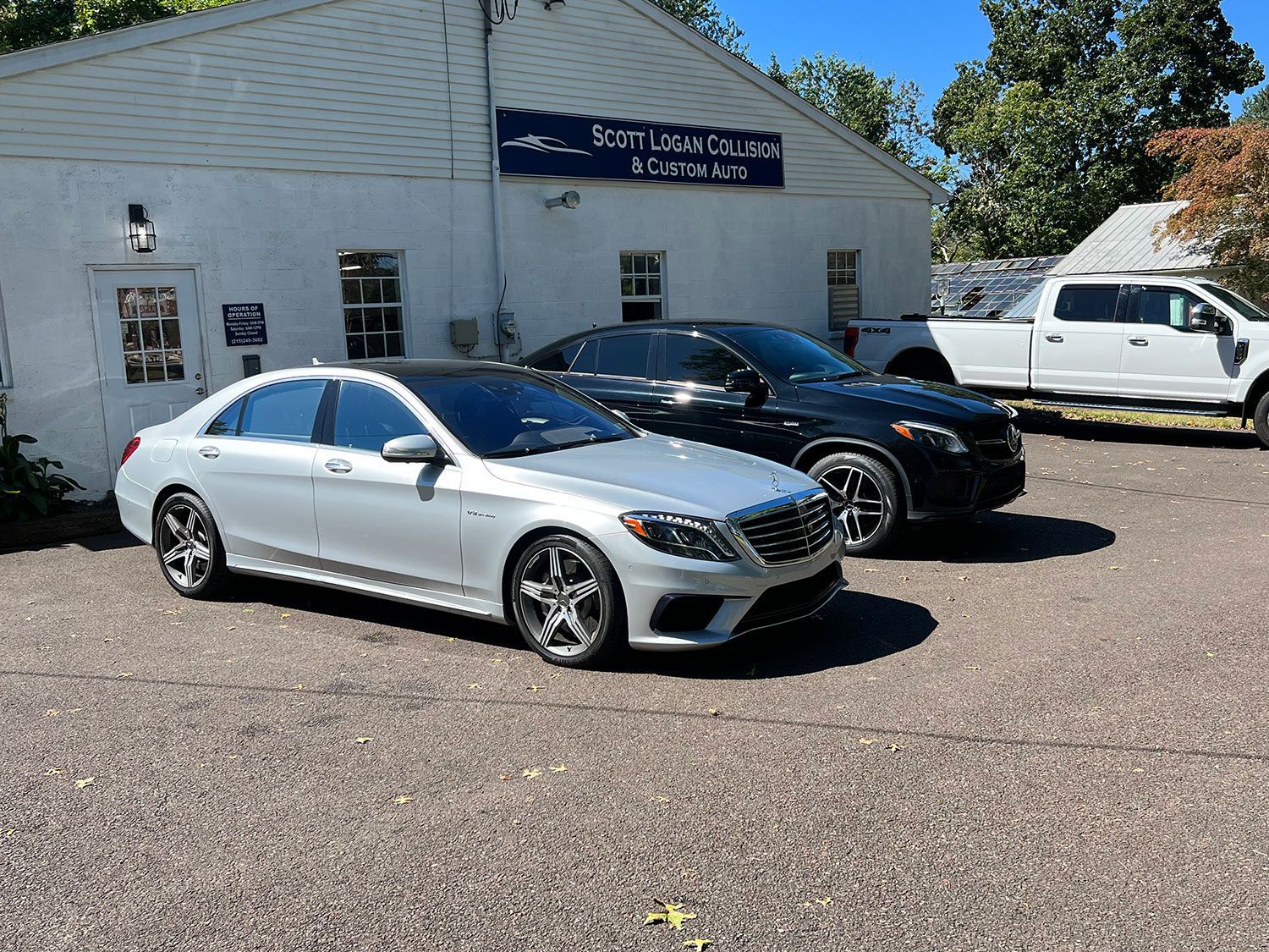 Silver Mercedes sedan parked in front of a white building with other cars.