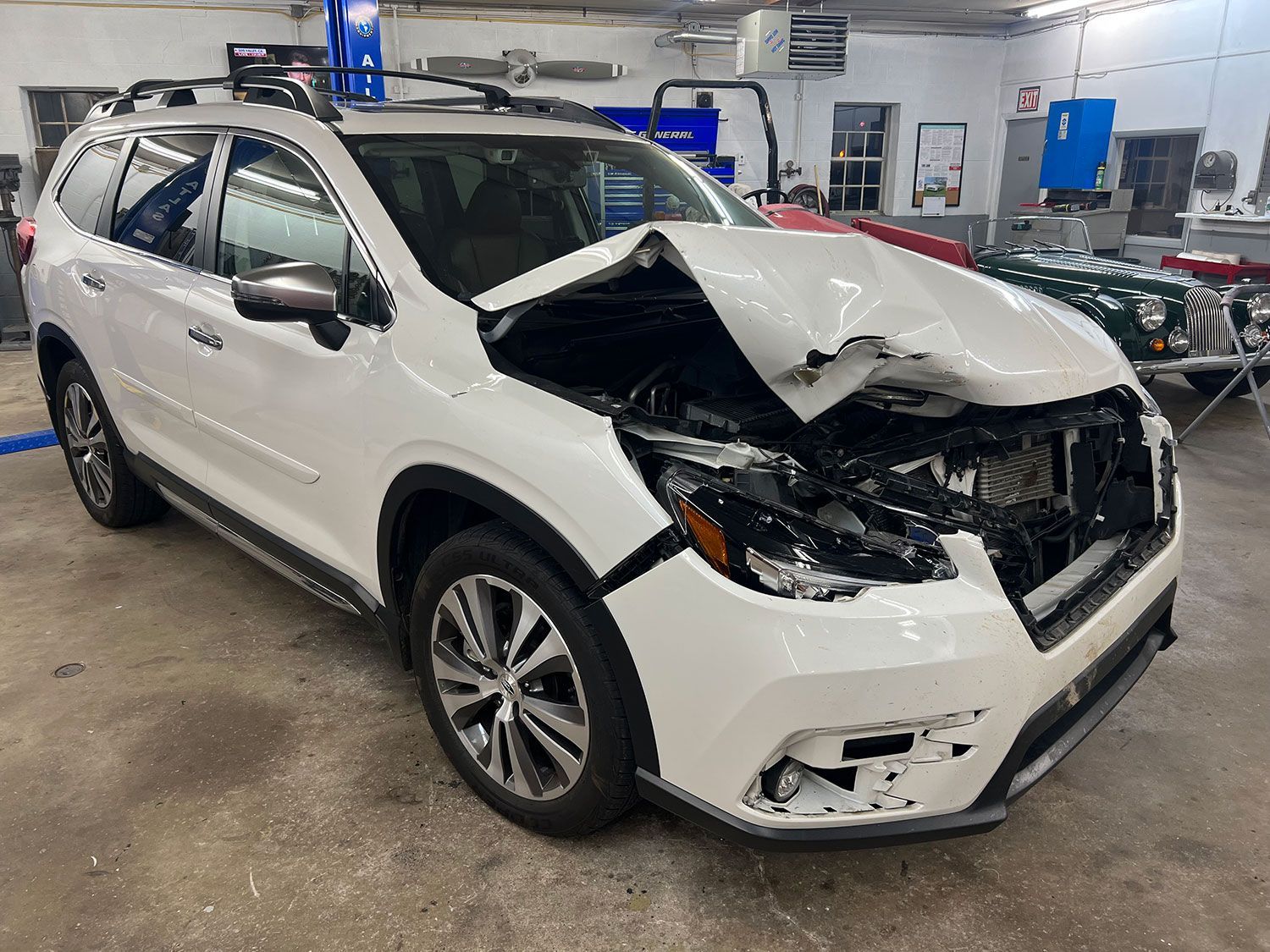White SUV with significant front-end damage in an auto repair shop.
