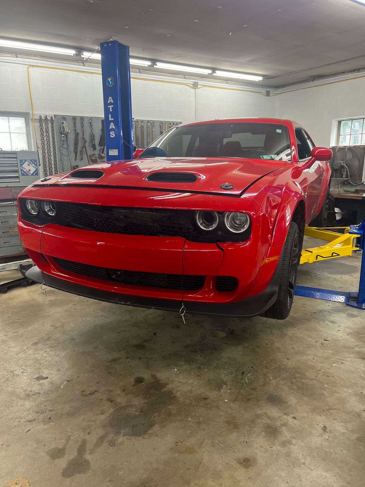 Red Dodge Challenger on a car lift in a garage.