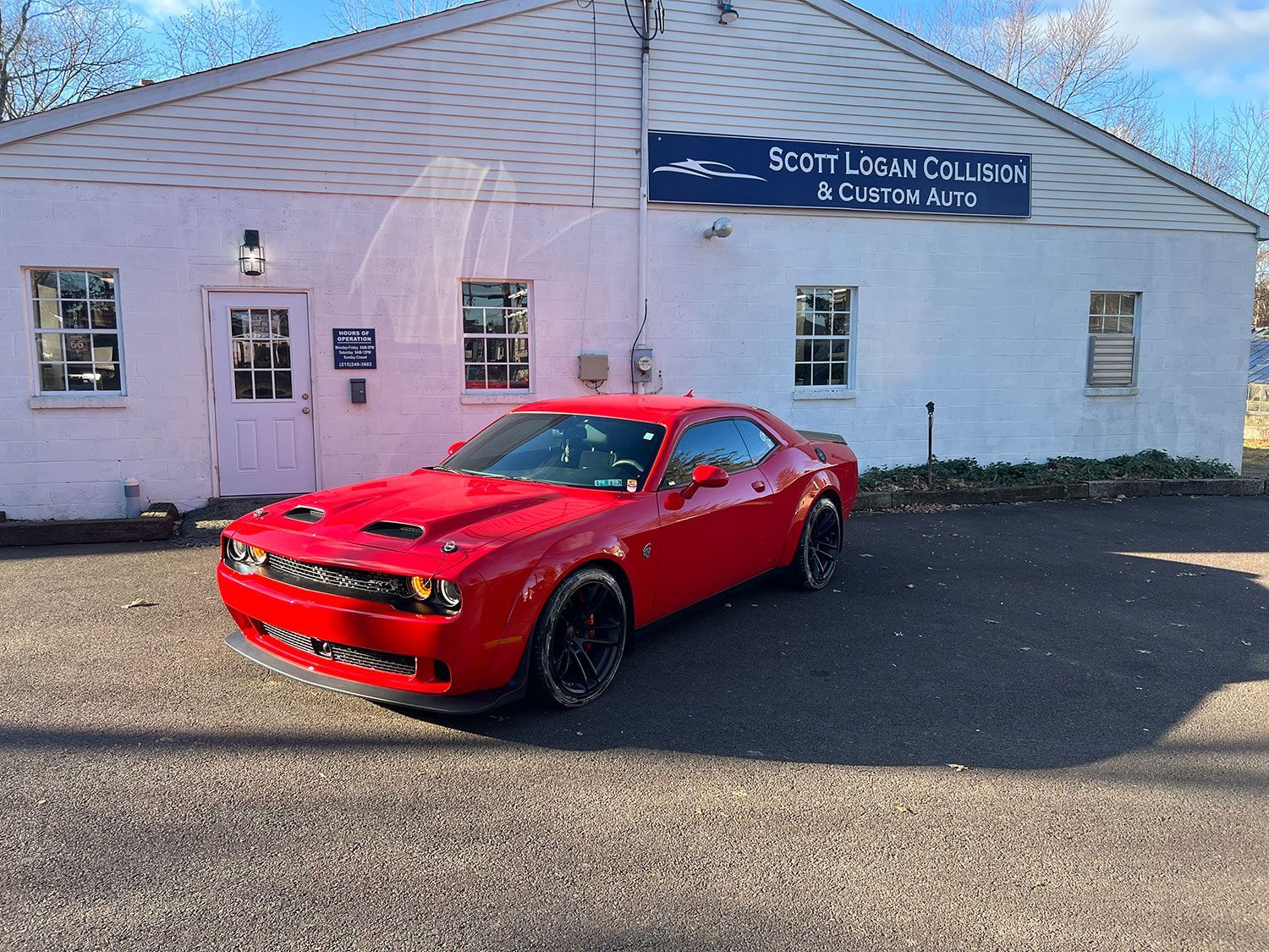 Red Dodge Challenger parked in front of a white building with a blue sign.