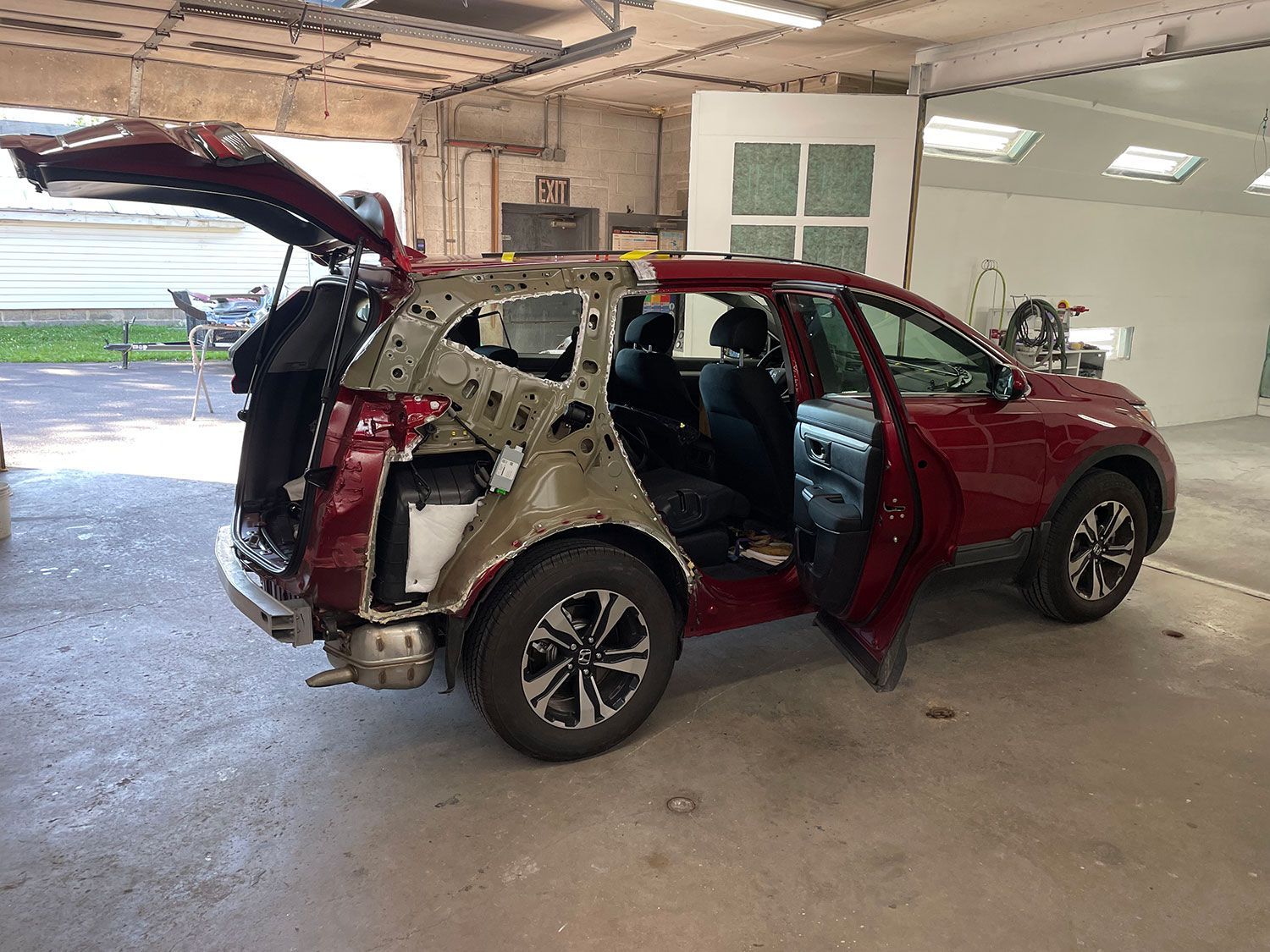 Red SUV with extensive body damage in a repair shop, doors open, rear hatch up.