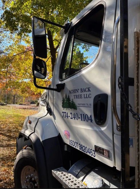 A side view of a white tree service truck featuring a logo and phone number, parked outdoors near trees in autumn.