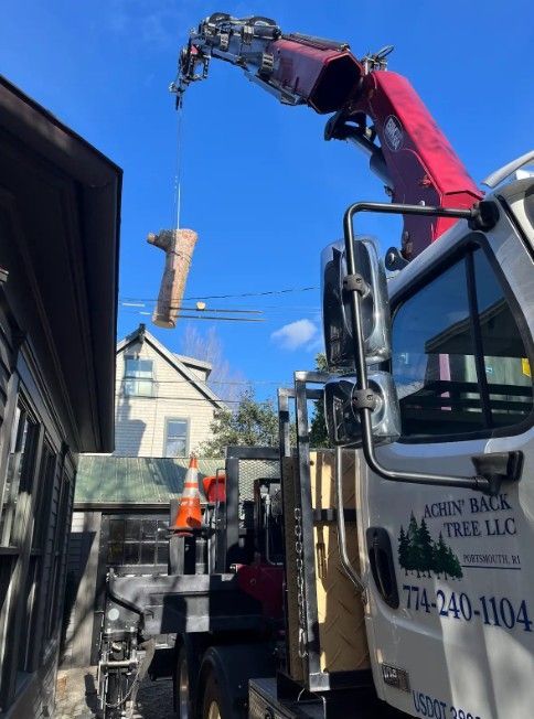A red boom crane lifting a large tree log into the air near a house, with the Acorn Rack Tree LLC logo on the truck cab.